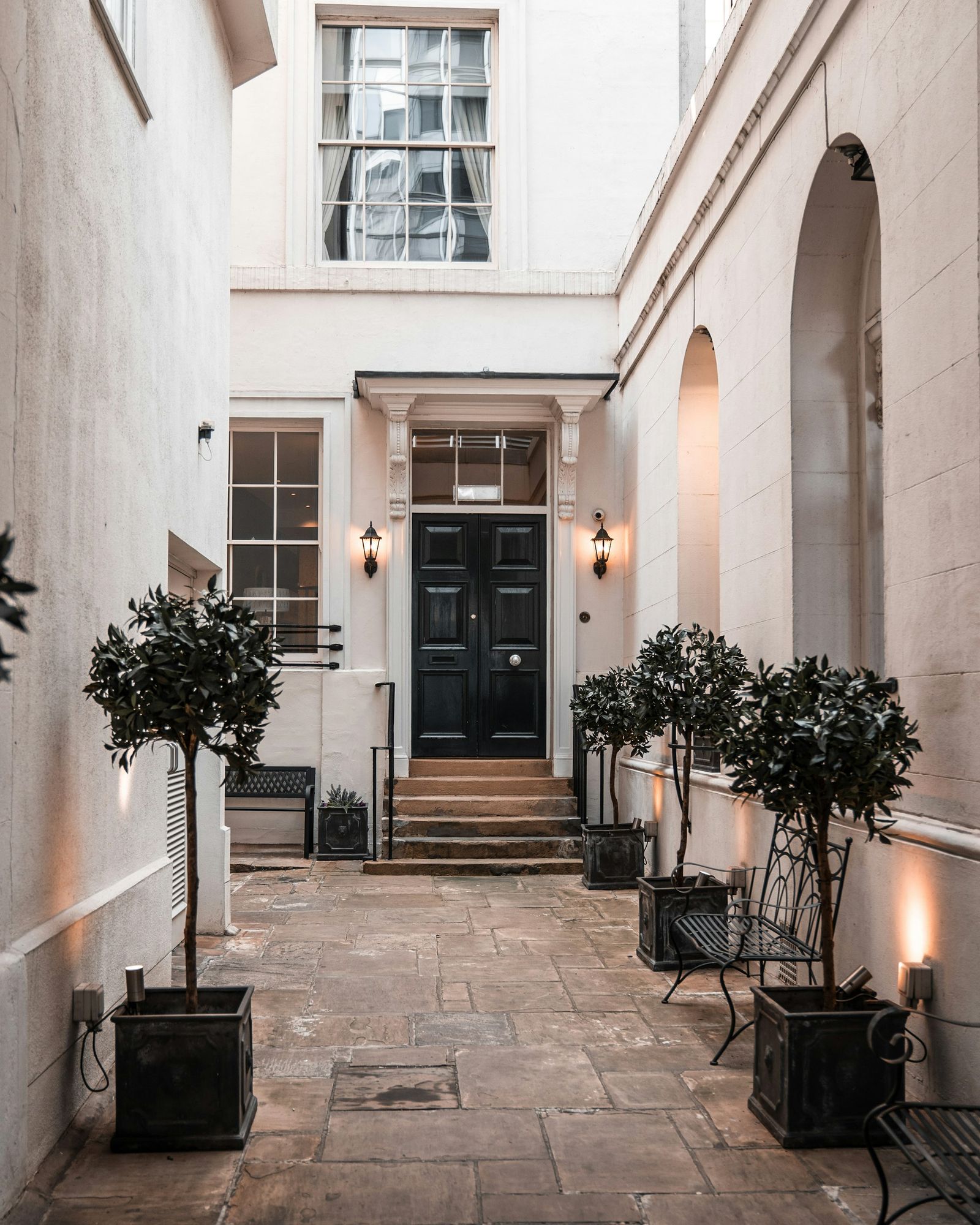 White stucco steps to a black front door between bay trees