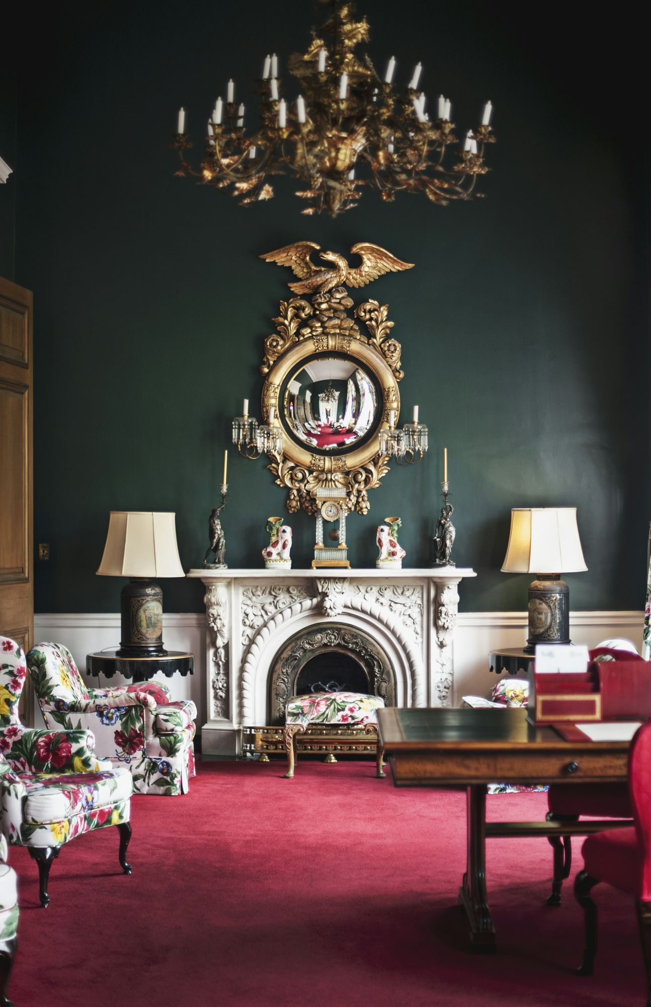 A dark green room with a gilt mirror over a marble fireplace