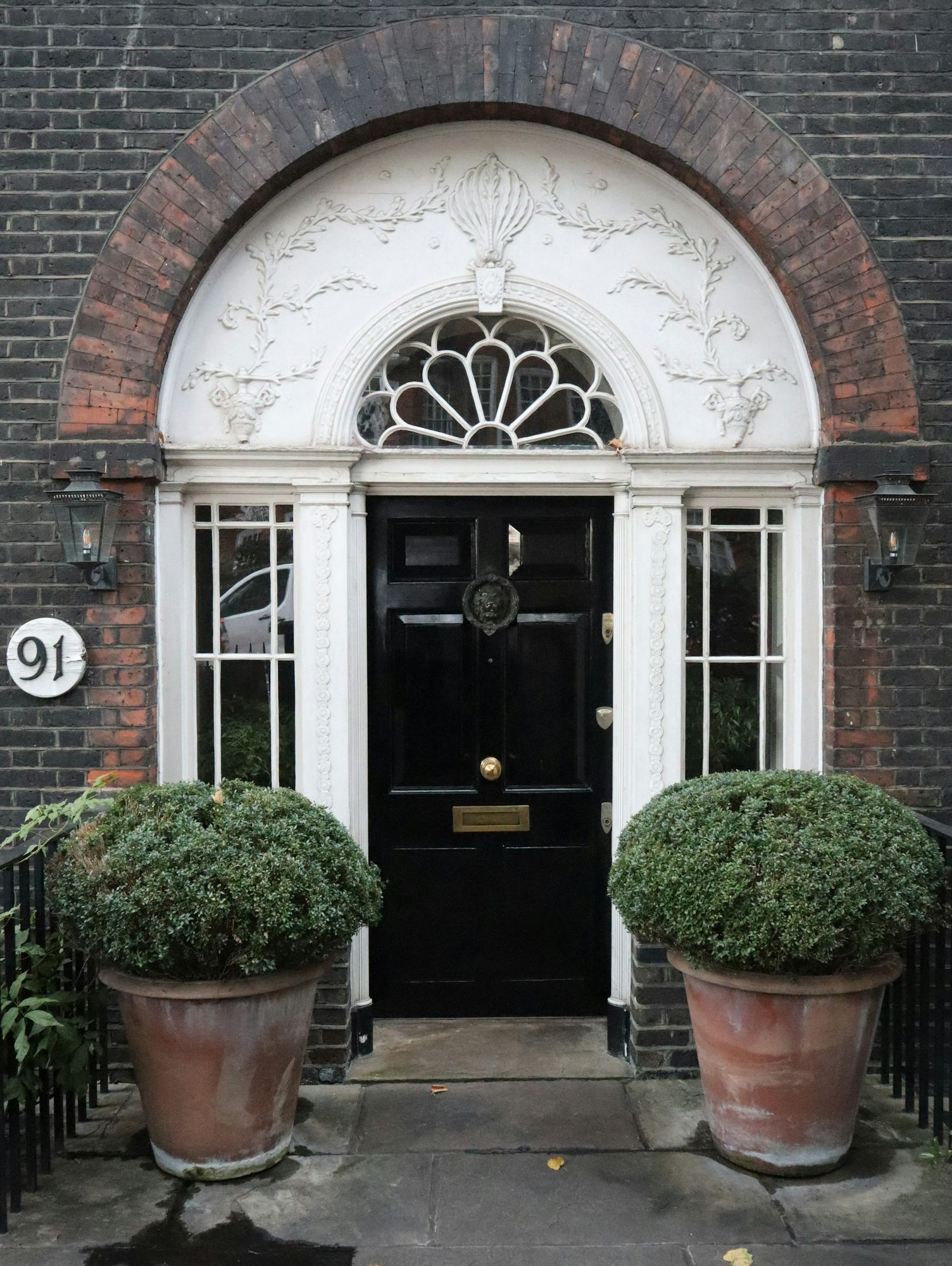 A black front door within a white portico and clipped box hedges